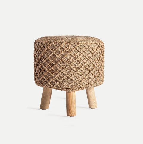 El reposapiés Puff en yute Gildeon es un puf redondo y tejido que presenta un diseño de cuerda texturizada y se apoya elegantemente sobre cuatro patas de madera sobre un fondo neutro, ofreciendo estilo y funcionalidad.