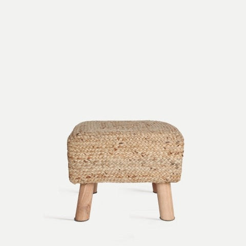 Puff reposapiés en yute THIESI, un pequeño puf de paja trenzada con cuatro patas de madera, irradia elegancia decorativa moderna sobre un fondo minimalista, que incorpora tanto estilo como comodidad.