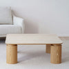 La Mesa de centro cuadrada en cerámico DM y fresno natural Línea realza un salón contemporáneo, elegantemente colocada sobre una alfombra beige y combinada con un sofá gris claro contra una pared lisa, mostrando la exquisita decoración del hogar.