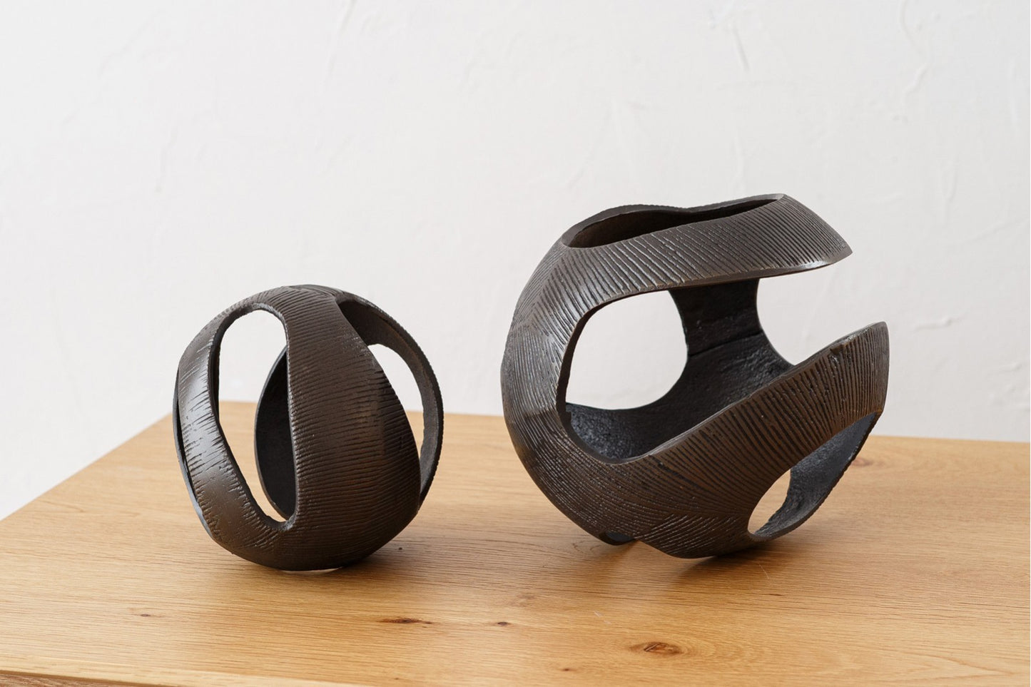 Dos esferas decorativas de metal con acabado en latón envejecido de la línea LUC añaden un toque impactante a cualquier conjunto decorativo al lucir sus elegantes bandas curvas sobre una superficie clara y fondo blanco.