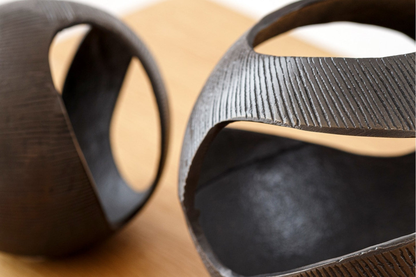 Dos esferas del set de 2 esferas decorativas de metal - latón envejecido - LUC, con acabados oscuros y recortes irregulares, reposan sobre una superficie de madera: piezas ideales para realzar la decoración moderna.