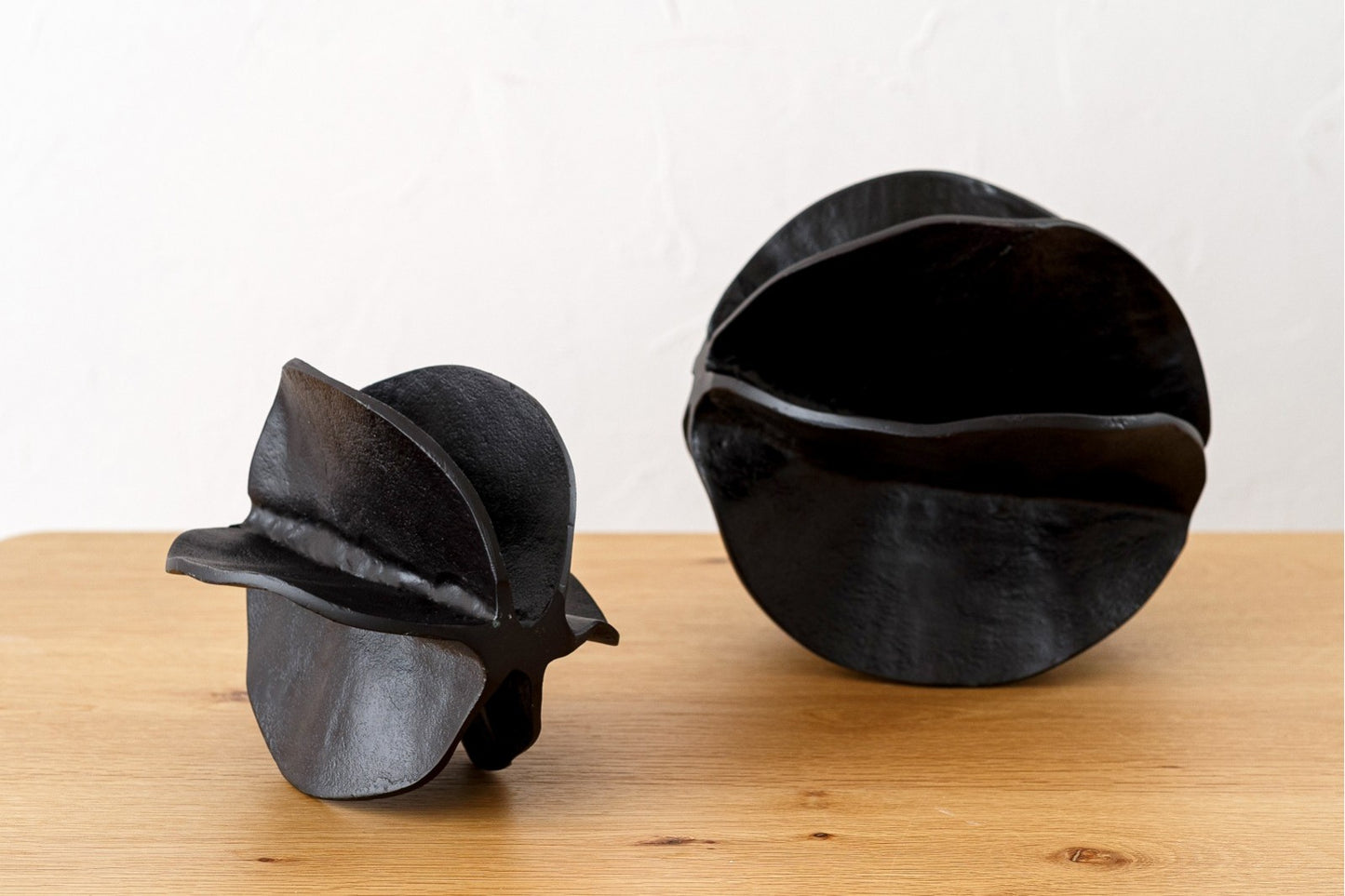 Dos abstractas esculturas decorativas de metal con textura de bronce oscuro del juego de 2 FRUTO se asientan sobre una superficie de madera clara sobre un fondo blanco liso.