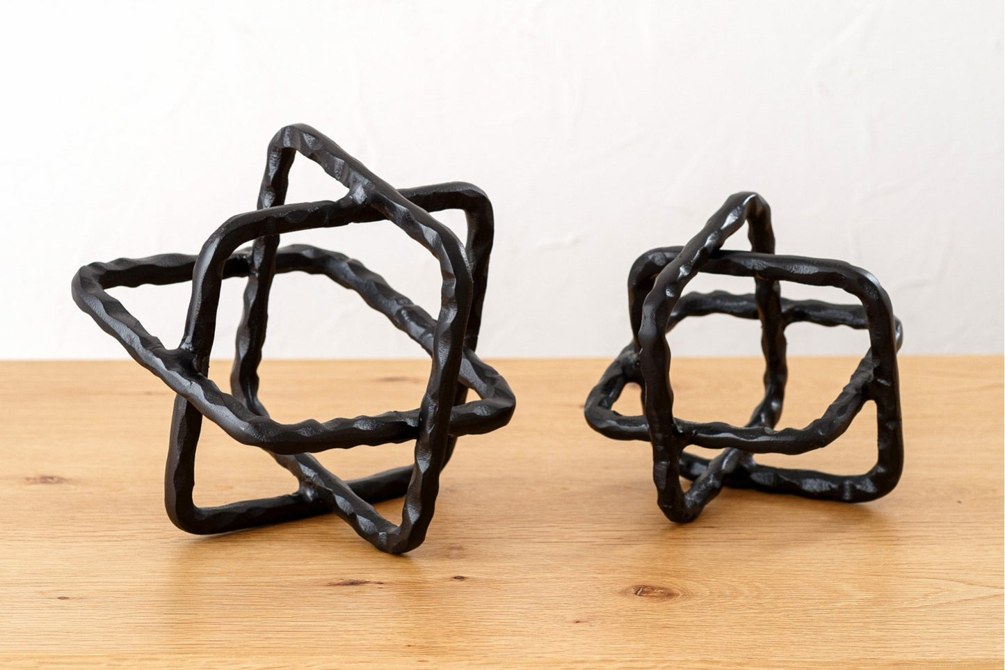 Dos esculturas decorativas de metal con acabado bronce oscuro rústico del set CUERDA se interconectan sobre una superficie de madera clara, ideales como piezas decorativas para espacios modernos.