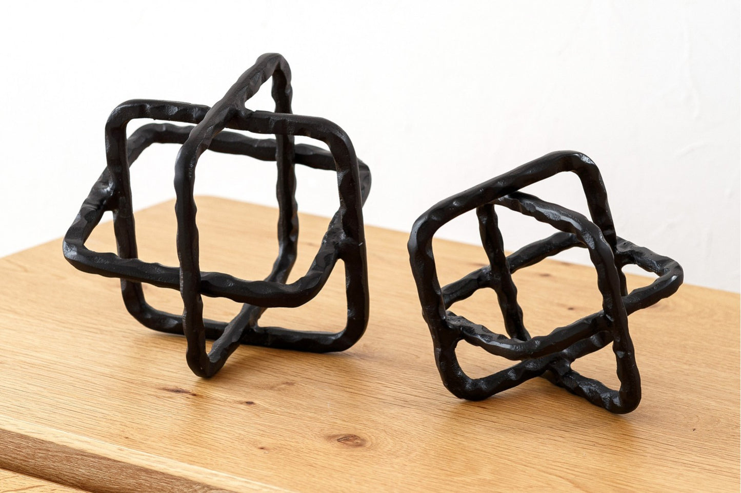 Dos esculturas decorativas de metal del set CUERDA, con acabado bronce oscuro rústico, se exhiben sobre una superficie de madera clara y fondo blanco, creando un llamativo conjunto decorativo.