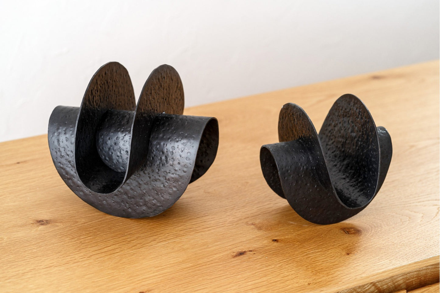 Set de 2 esculturas decorativas de metal ONDA en bronce envejecido texturizado, de diseño abstracto y curvo, expuestas sobre una superficie de madera clara con fondo neutro.