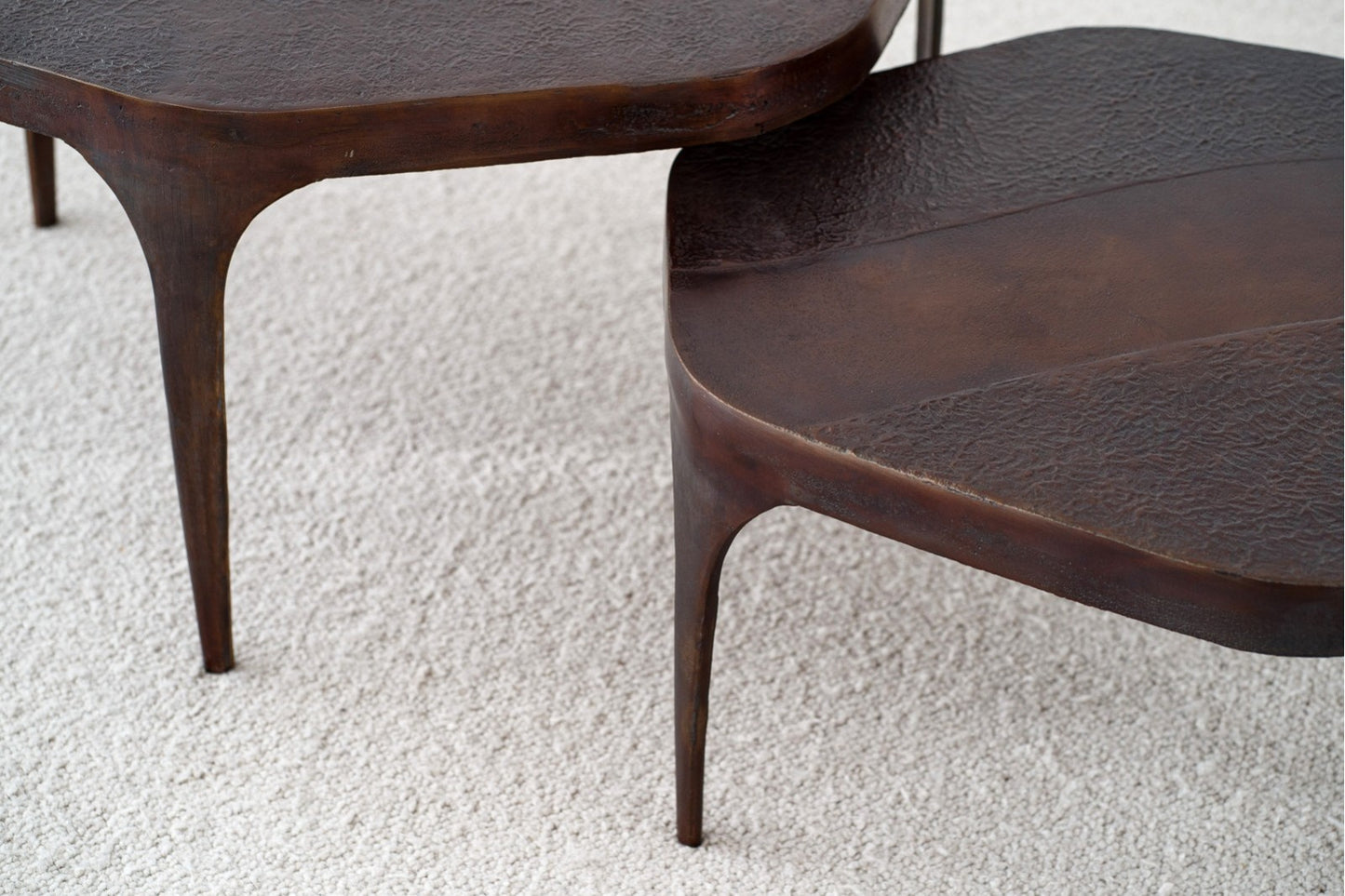 Dos mesas de centro redondas de metal oscuro con un acabado artesanal de óxido (Set de 2 mesas de centro NAIN) y patas esbeltas se apoyan sobre una alfombra clara y texturizada, aportando un toque industrial.