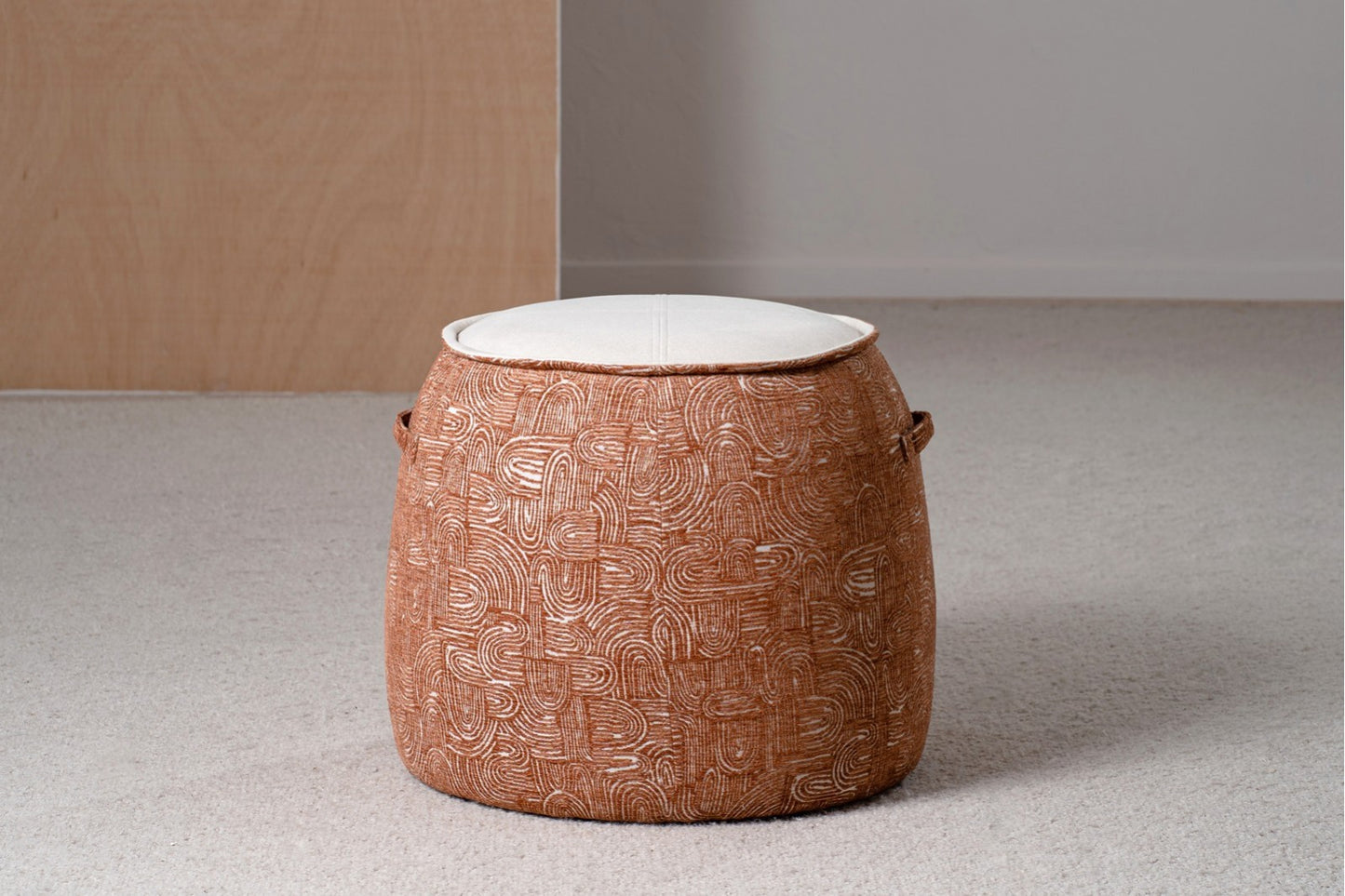 Dos pufs redondos EREA tapizados en teja y marfil (50×50×40 cm), con asas laterales y vivo doble de estilo contemporáneo, se ubican sobre una alfombra clara junto a una pared de madera.