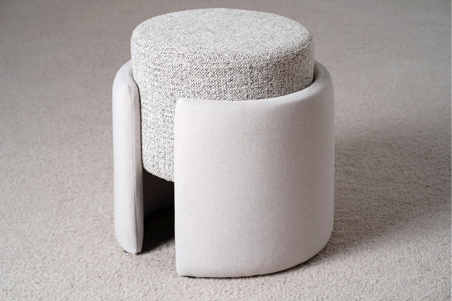 Juego de 2 pufs redondos contemporáneos, tapizados en tela bicolor marfil y gris (42,5×41×45 cm), de la colección XANA, con asiento texturizado y laterales curvos acolchados, expuestos sobre un suelo de moqueta clara.