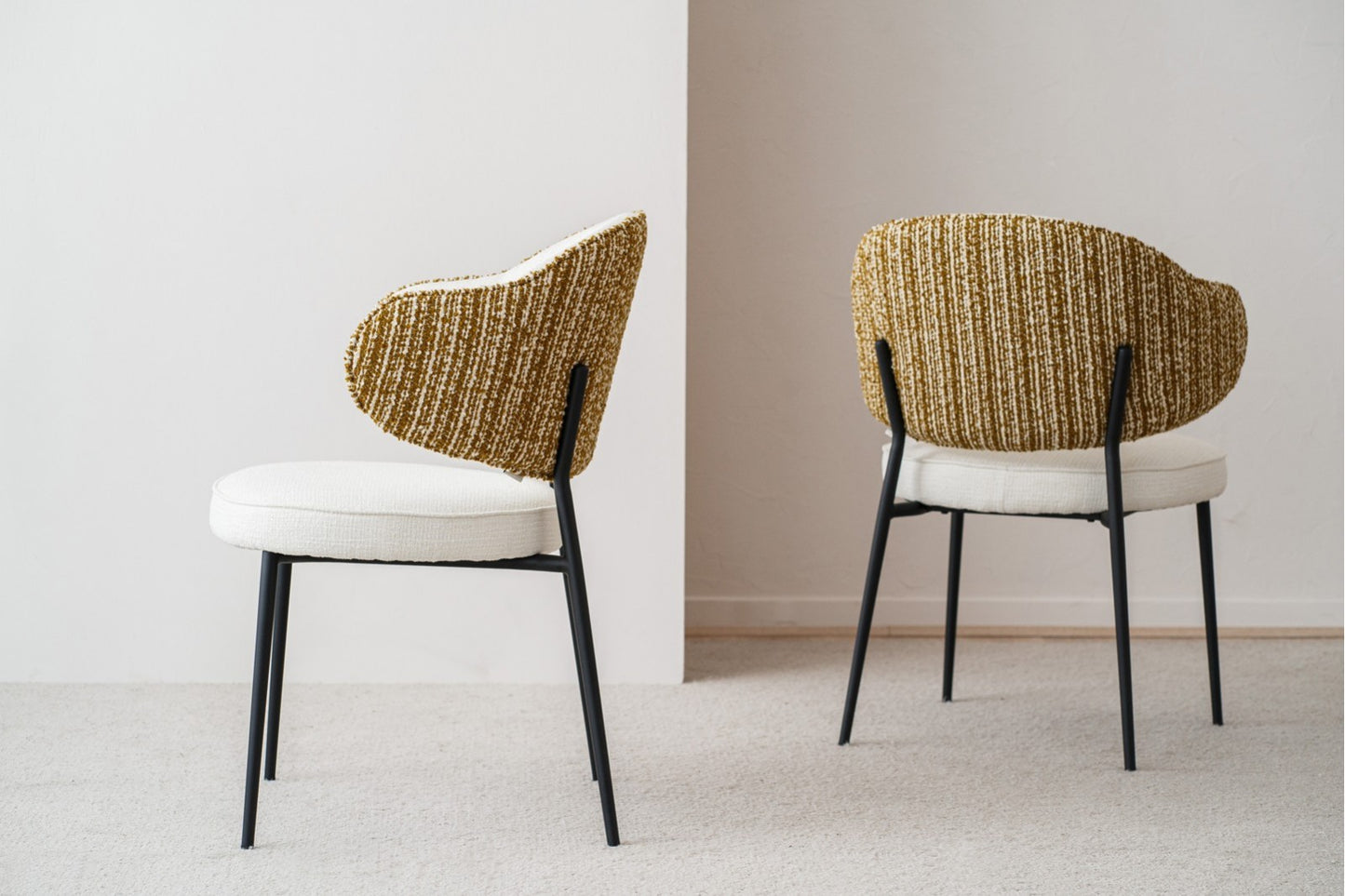 El set de 2 sillas de comedor CLOE, tapizadas en blanco y mostaza (58,5×58×82 cm) con patas de metal negro y diseño contemporáneo, está ubicado junto a una pared blanca sobre un suelo claro.