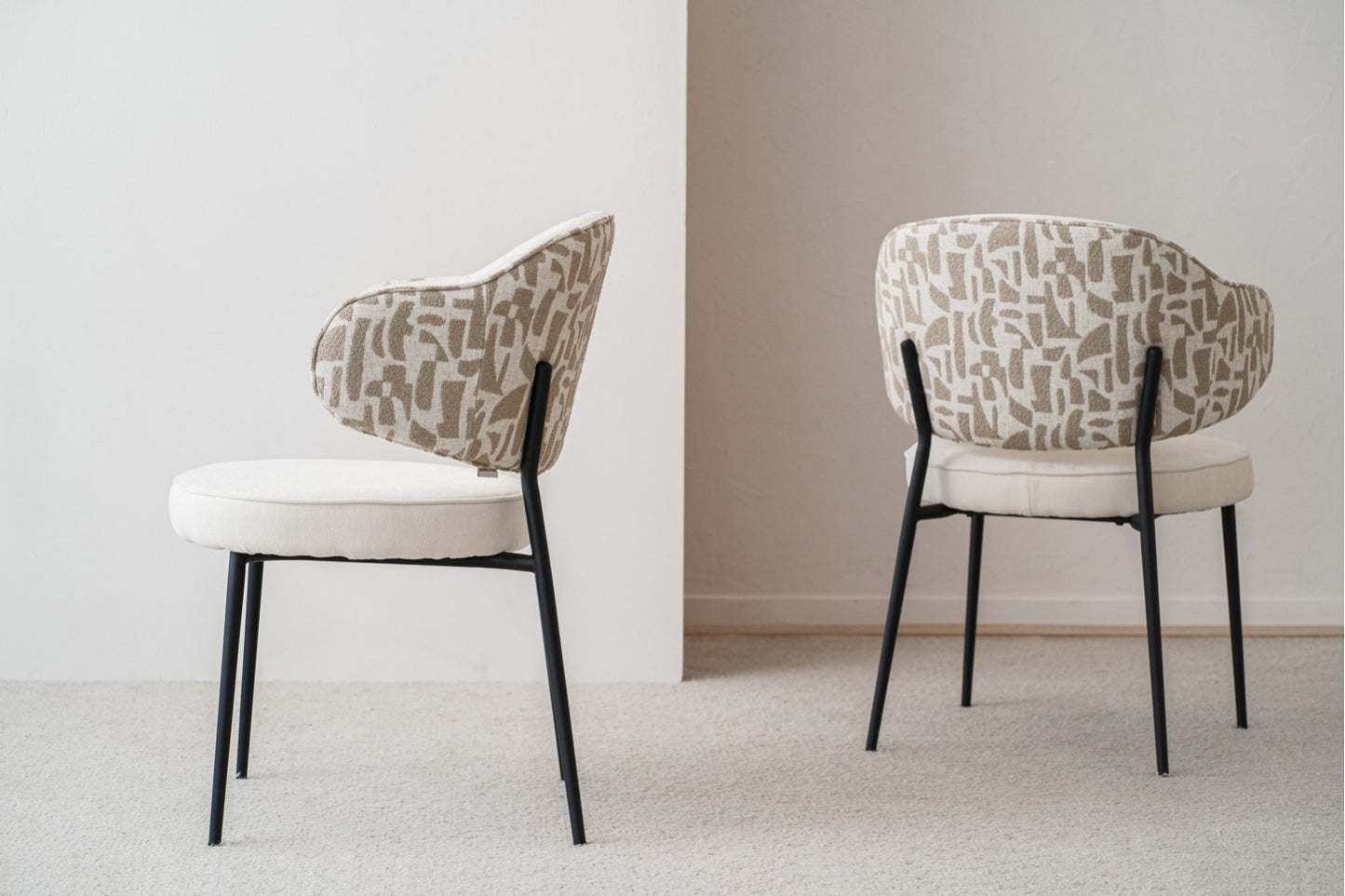El set de 2 sillas de comedor CLOE, tapizadas en beige y piedra (58,5×58×82 cm) con patas de metal negro, está dispuesto sobre una alfombra clara en una habitación minimalista.