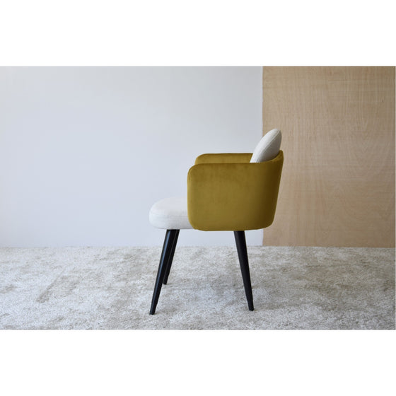 Una silla moderna con patas negras, asiento blanco y respaldo color mostaza se coloca sobre una alfombra beige texturizada sobre un fondo minimalista. Esta elegante pieza forma parte del Pack de 2 Sillas de Comedor con Brazos, Verde Ocre y Beige - Eleganzia.