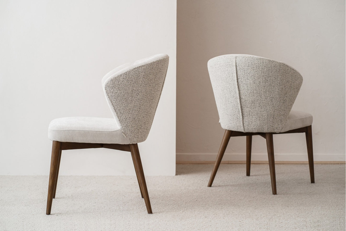 Un set de 2 sillas de comedor tapizadas en beige y gris (61×62×84 cm), con estructura de madera nogal y estilo contemporáneo EVA, está colocado sobre una alfombra frente a un fondo neutro.