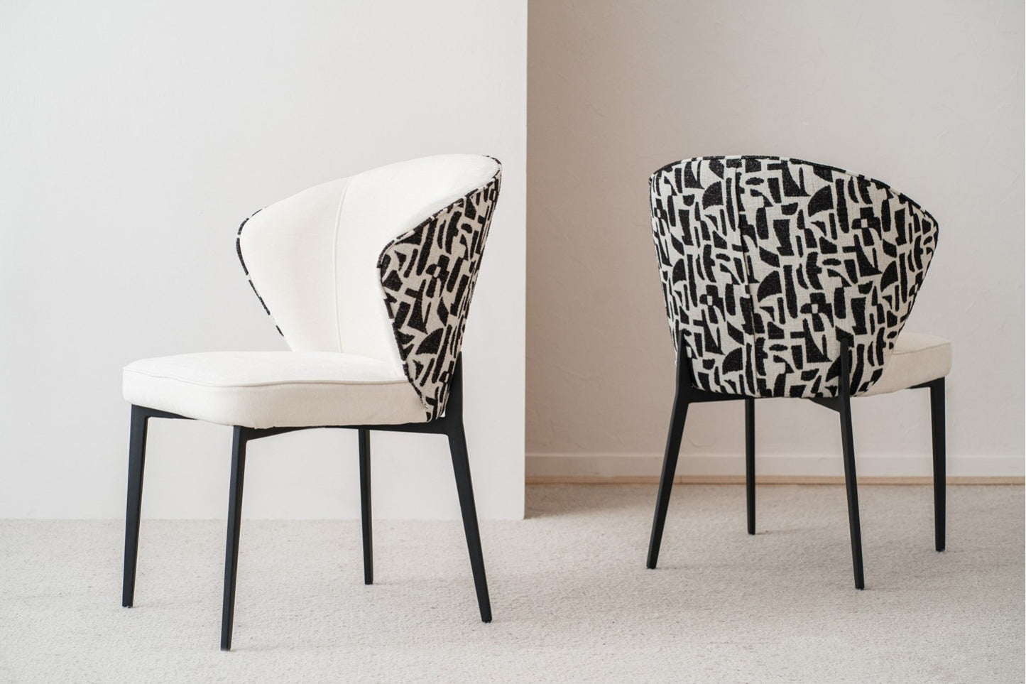 Set de 2 sillas de comedor EVA, tapizadas en beige y negro (61×63×86 cm) con patas de metal negro, diseño contemporáneo; una con frente liso beige y otra con respaldo estampado abstracto. Fondo minimalista.