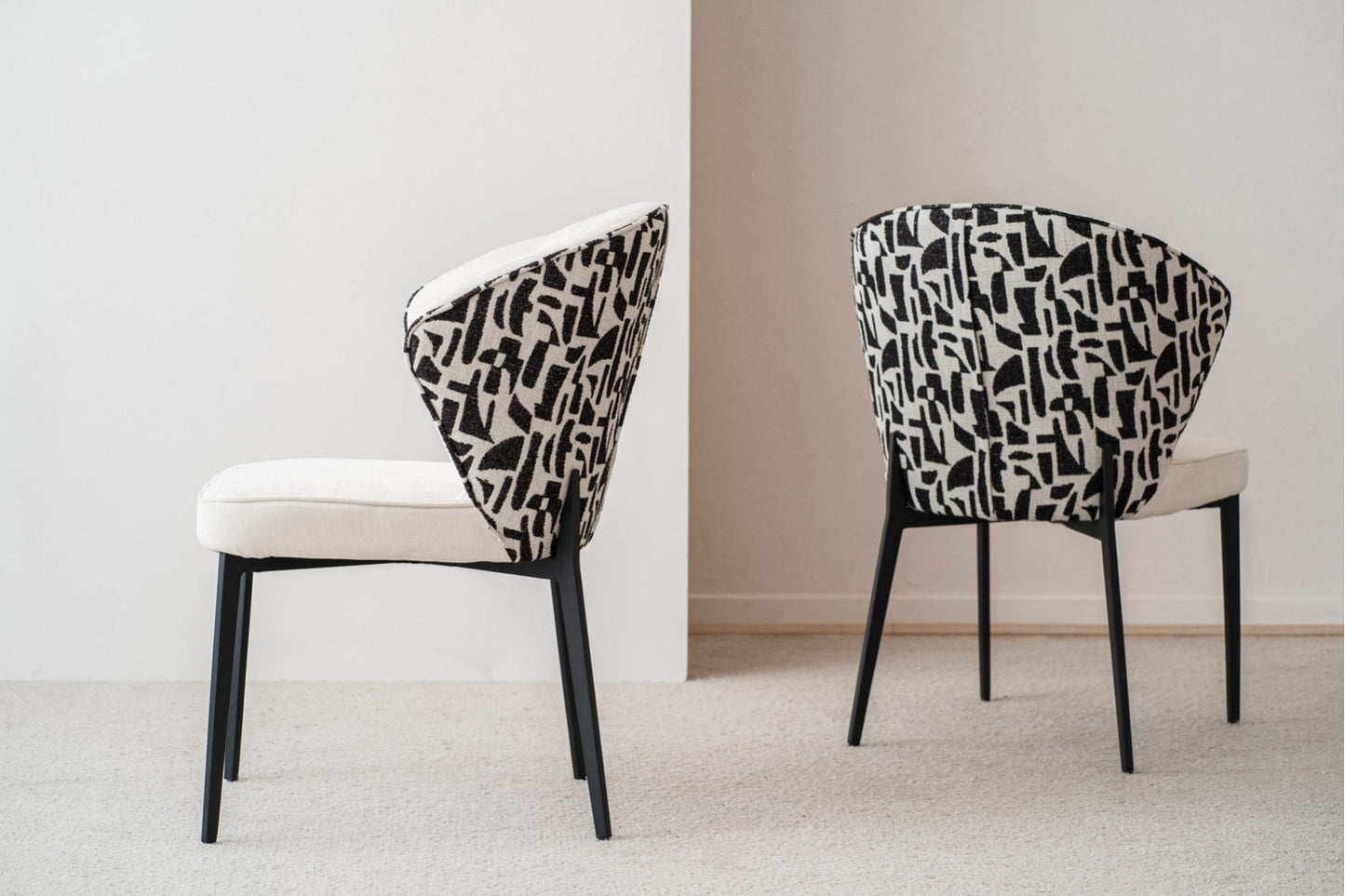 Set de 2 sillas de comedor EVA, tapizadas en beige y negro con base de metal negro (61×63×86 cm), estilo contemporáneo, lucen elegantes sobre una alfombra clara frente a una pared neutra.