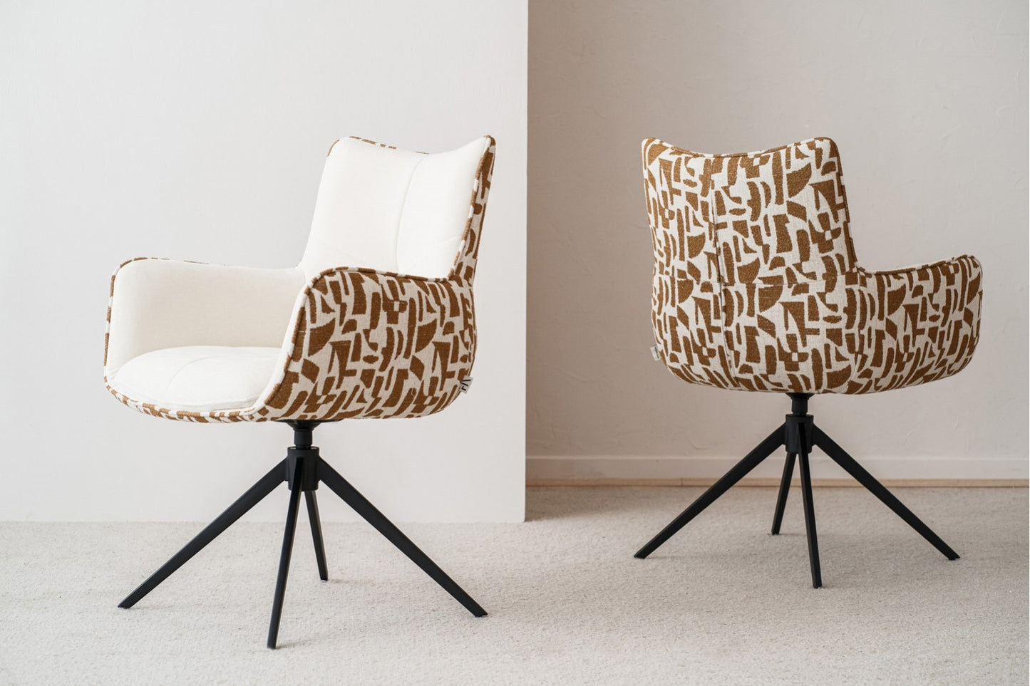 El set de 2 sillas de comedor giratorias SAEL, tapizadas en beige y ocre con brazos y patas de metal negro, mide 61×63×86 cm y luce un estilo contemporáneo sobre una alfombra clara junto a una pared neutra.