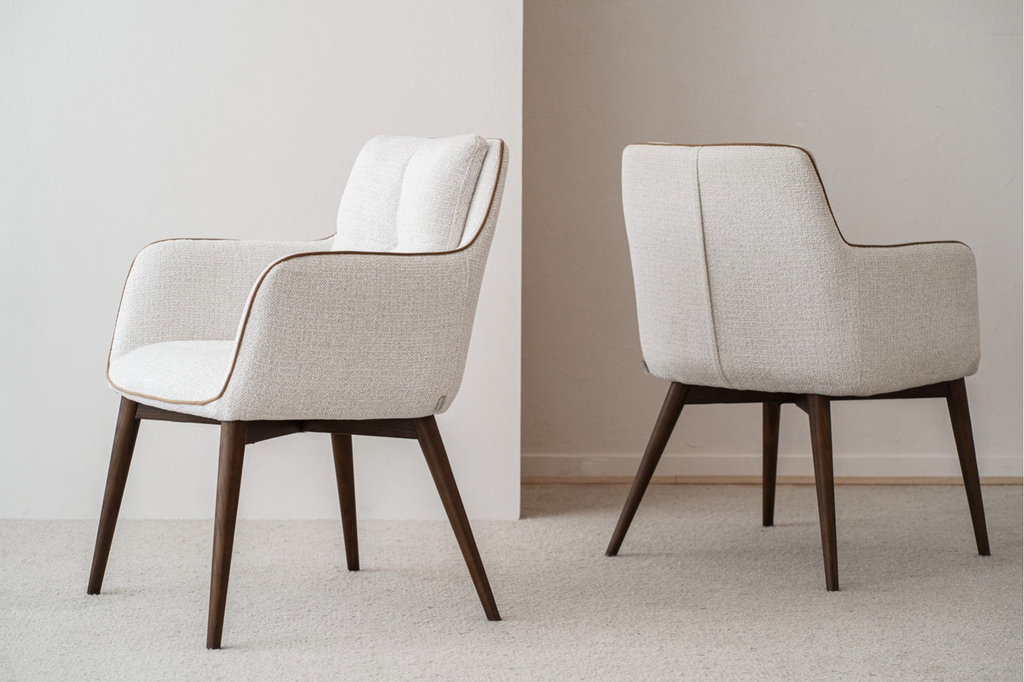 El set de 2 sillas de comedor OLIVER, con brazos tapizados en tono marfil y patas de madera nogal (61×67×86 cm), estilo contemporáneo, está ubicado sobre una alfombra frente a una pared neutra.
