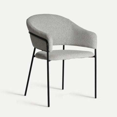 La silla de comedor de poliéster y metal Bikal, con su tapizado gris, respaldo redondeado y patas de metal negro, irradia el encanto del estilo vintage de un comedor. Su diseño atemporal destaca sobre un fondo blanco liso, ideal para quienes buscan muebles con carácter.