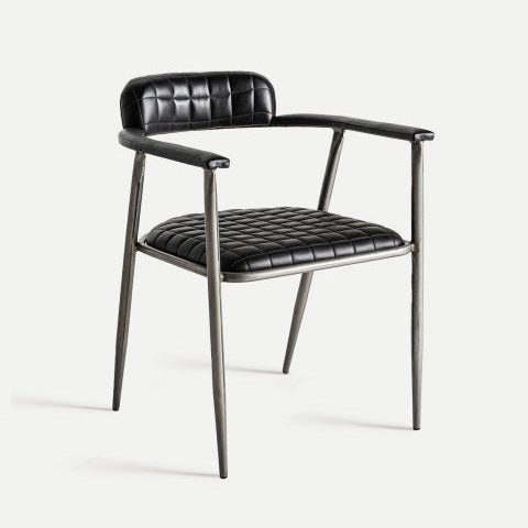 La silla de comedor tapizada en piel Olby cuenta con asiento y respaldo de cuero negro acolchado. Sus patas y reposabrazos metálicos ofrecen un diseño vintage, sobre un fondo blanco liso.
