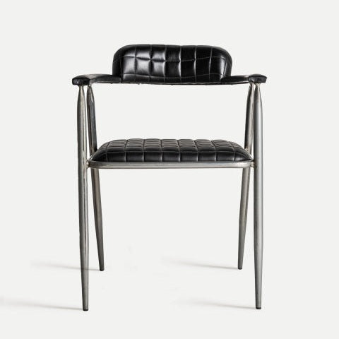 La silla de comedor tapizada en piel Olby presenta un diseño vintage con un patrón de cuero negro acolchado, un elegante marco de acero inoxidable, respaldo bajo y apoyabrazos.