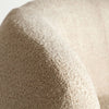 Primer plano de un tejido bouclé crema texturizado sobre una superficie curva, probablemente el Sillón tapizado en bouclé crema Privas, que muestra su apariencia suave y tejida que exuda un diseño elegante.