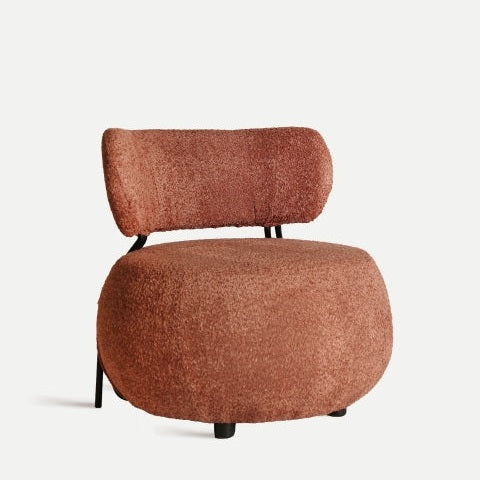 El sillón tapizado en bouclé Valence cuenta con asiento redondeado, respaldo curvo y tapizado en tejido bouclé de algodón color óxido, ideal para aportar un toque elegante a la decoración art deco.