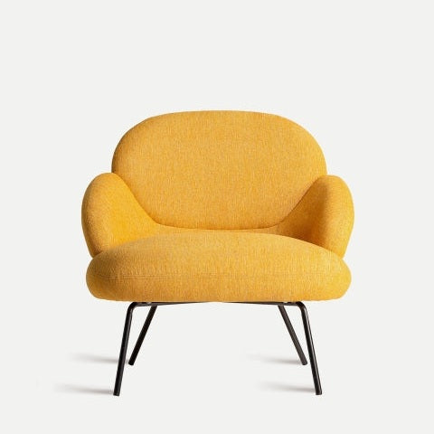 El sillón de chenilla mostaza Dokkum exhibe una sofisticación moderna con su tapizado en mostaza, respaldo y brazos redondeados y elegantes patas de metal negro, elegantemente colocadas sobre un fondo blanco liso.