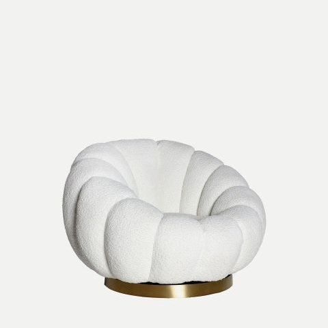 El sillón giratorio de algodón bouclé Crest es un sillón blanco de felpa con un diseño redondeado, que presenta detalles segmentados y una base circular de latón, sobre un fondo claro y liso.