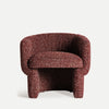 El Sillón tapizado jaspeado Leke, un sillón de tela roja con textura, presenta un respaldo redondeado y un cojín de asiento grueso con elegancia y comodidad sobre un fondo liso y claro.