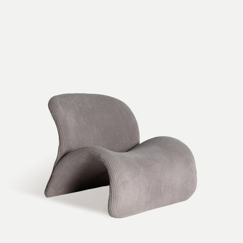El Sillón moderno tapizado gris Vianne es un sillón curvo con una textura acanalada que encarna el estilo Art Decó sobre un fondo liso y pálido.