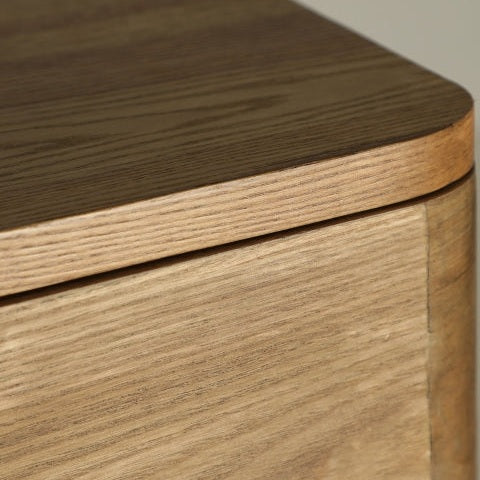 Primer plano de la esquina de la cómoda en madera DM marrón Hoek, resaltando sus bordes suaves y redondeados, veta de madera visible y un toque de diseño contemporáneo.