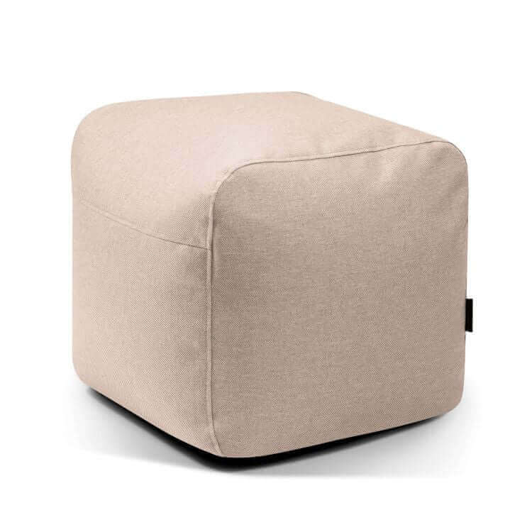 El Pouf Plus 50 Riviera, una otomana cúbica de tela beige con bordes redondeados para exteriores, sirve de asiento adicional ideal y se muestra sobre un fondo blanco liso.
