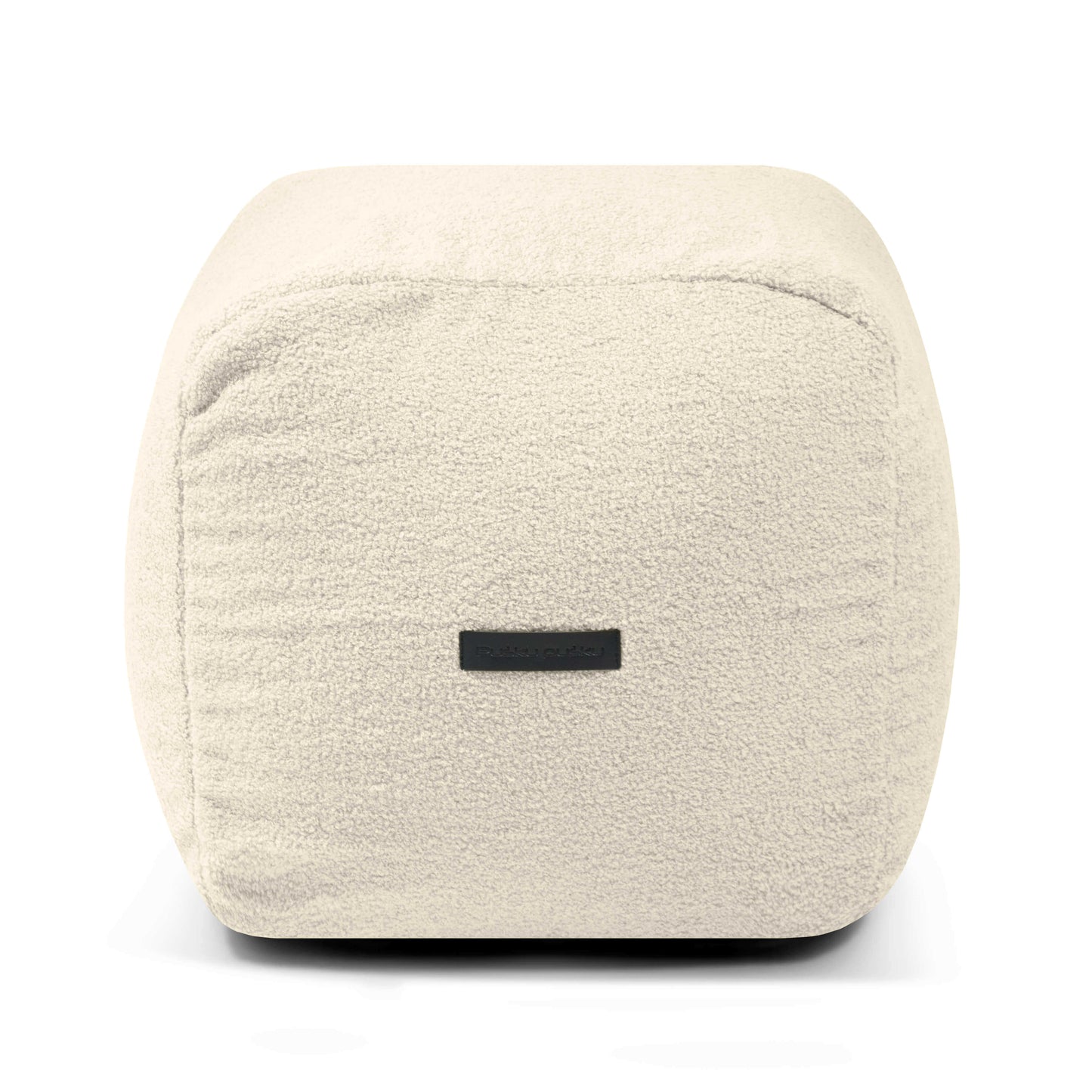 El PLUS 50 TEDDY es un puf cuadrado compacto y ligero (50×50×35 cm) en tejido sherpa color crema con una pequeña etiqueta negra, perfecto para dormitorios o cuartos de juegos modernos, mostrado sobre un fondo blanco.