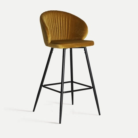 El Taburete alto 74 cm en terciopelo y metal Algio es un taburete de bar en terciopelo ocre, que presenta un respaldo curvado y elegantes patas de metal negro con reposapiés, que rezuma elegancia Art Decó.