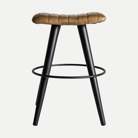 El Taburete en piel y metal Befaux presenta patas de cuero marrón y metal negro con un reposapiés circular, encarnando el diseño industrial contemporáneo.