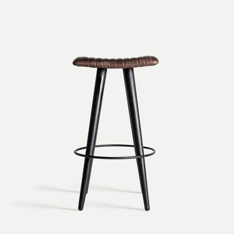 El Taburete alto 74 cm en piel y metal Befaux es un taburete negro de tres patas con asiento de cuero marrón, que presenta un reposapiés circular cerca de la base, que exuda un diseño industrial vintage.