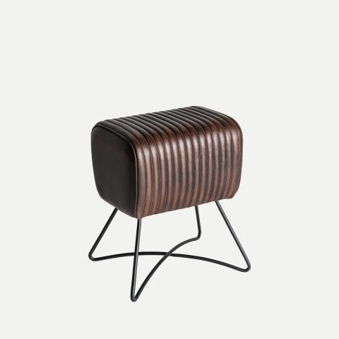 El Taburete bajo en piel Gladys, un asiento rectangular acanalado de color marrón oscuro con patas de metal negro, encarna el diseño industrial moderno sobre un fondo liso, ideal para cualquier cocina abierta.