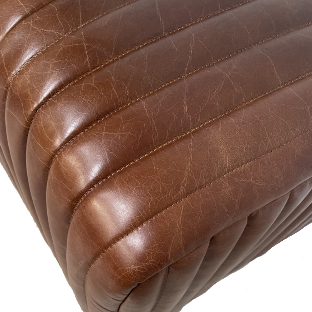 Primer plano del Pouf cuadrado cuero marrón Bristol con su superficie de cuero marrón, presenta costuras verticales, pliegues visibles y un acabado pulido texturizado.