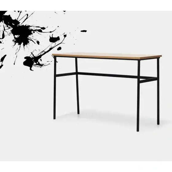 Una sencilla mesa de madera con patas de metal negro se alza sobre un fondo blanco con salpicaduras de tinta negra en el lado izquierdo, encarnando un diseño minimalista ideal para despachos y salas de trabajo.