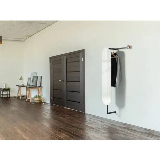 Una decoración de diseño minimalista con un espejo Zyzy, una puerta oscura, un perchero montado en la pared con una bolsa y chaqueta, un monopatín, y una pequeña.